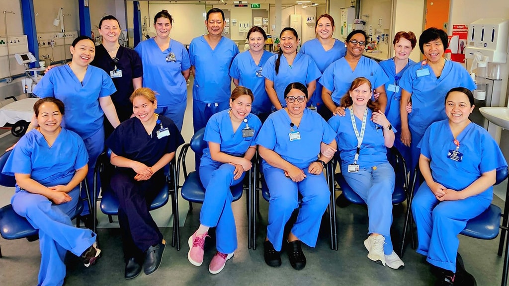 Group of female and male nurses standing on a stair case in a hospital setting smiling